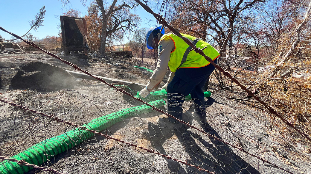 Delta_Emergency_SiltSockThruWire_101025_1040x585 corpsmember in safety vest lays out a green silt sock, with barbed wire in the foreground
