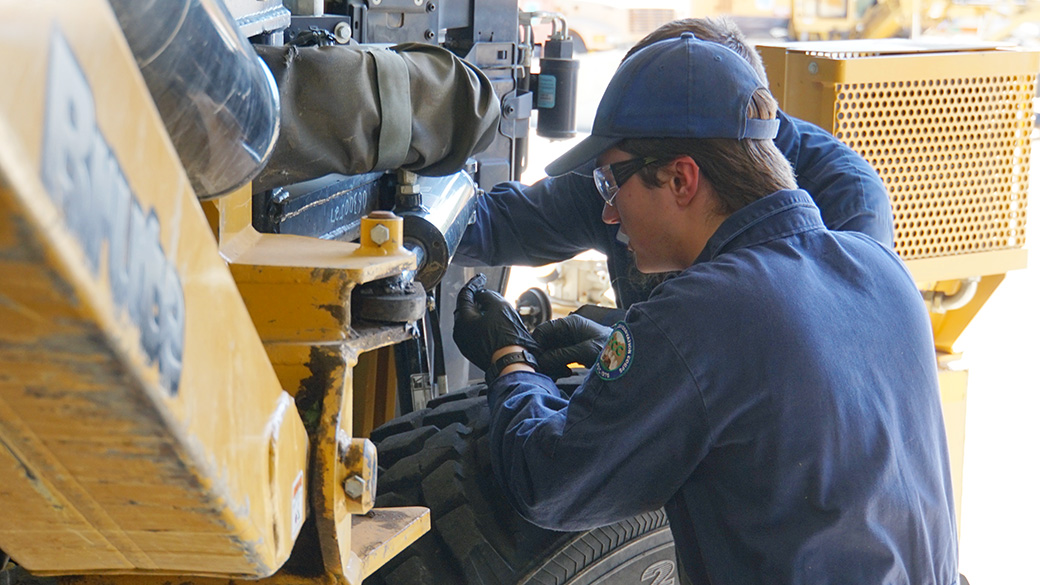 LosPadres_CaltransMechanic_RoryMowerRepair_082125_1040x585 male in blue hat and coveralls working on a large mower in a garage