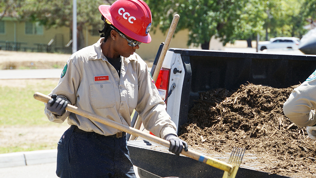 female corpsmember unloads mulch from the back of a pick up