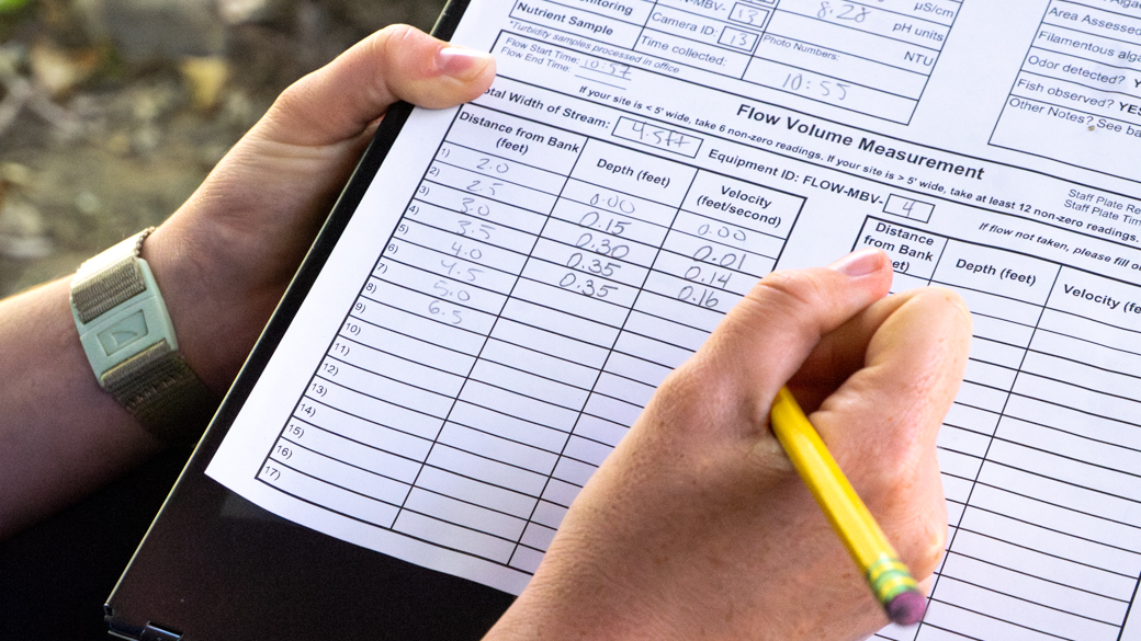 Hands recording the distance, depth, and velocity of a creek in San Luis Obispo.