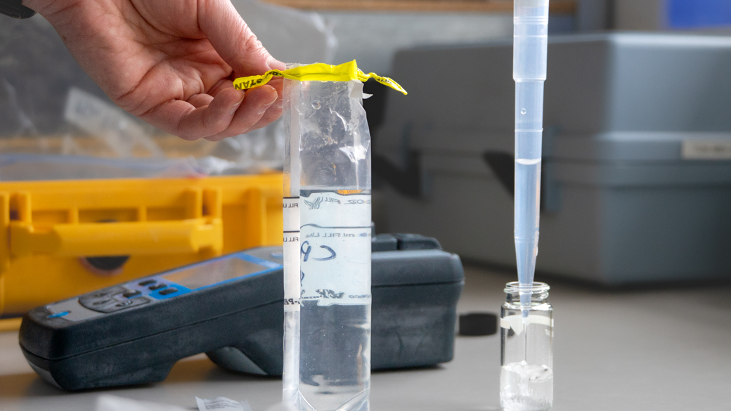 Close up of a syringe dispensing a water sample from a creek into a testing vial.