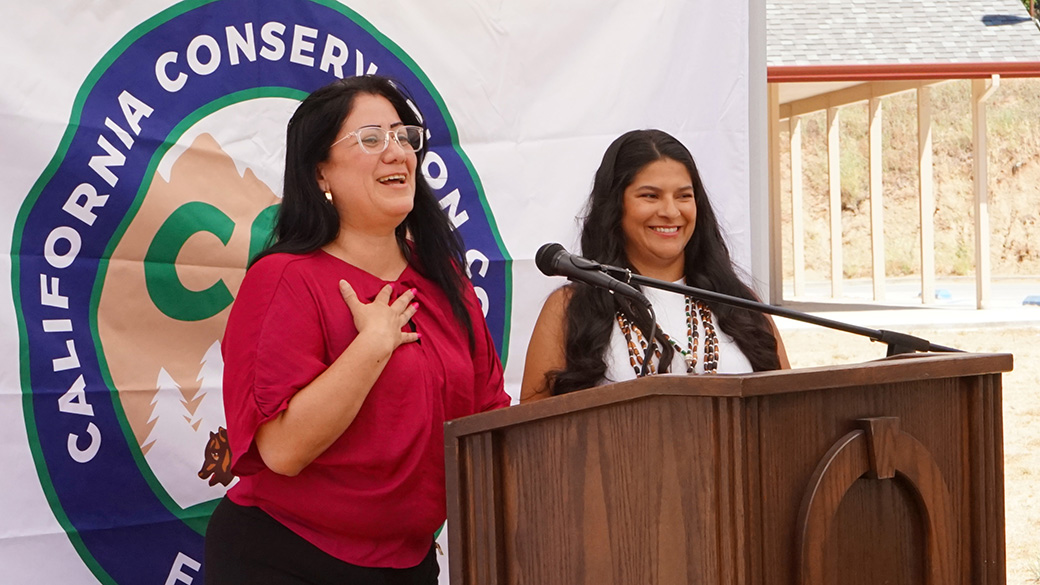 two females at a microphone with CCC logo in the background at podium