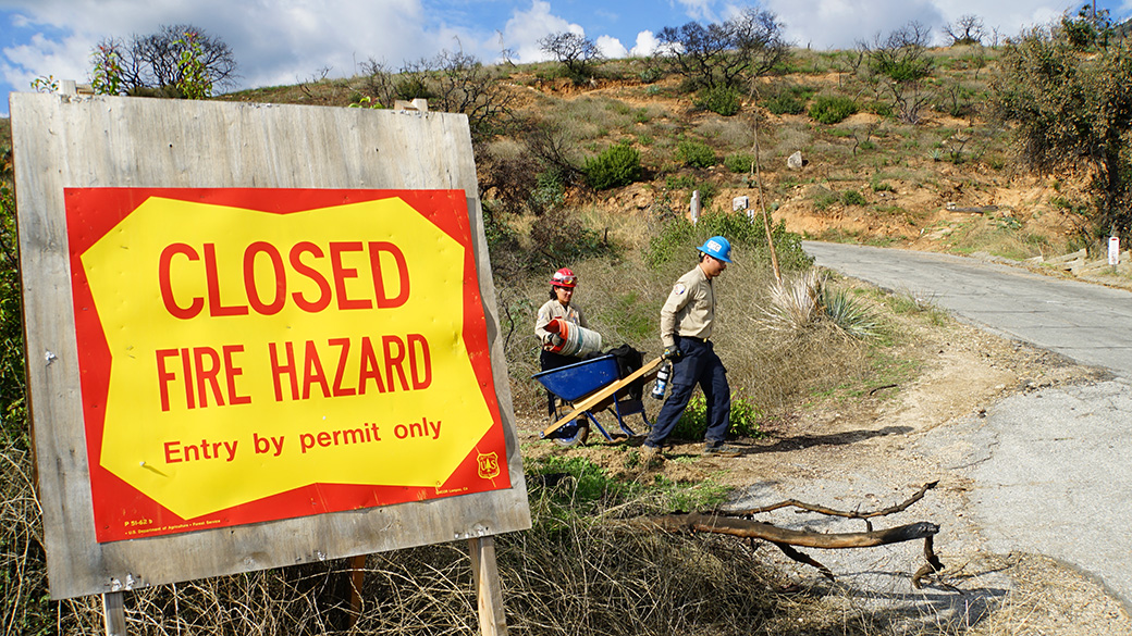 corpsmembers haul out equipment from trail behind a sign that reads closed fire hazard