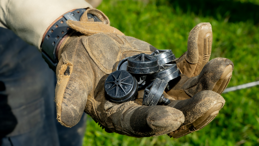 A Corpsmember holds up emitters that help control the flow of water in irrigation lines.