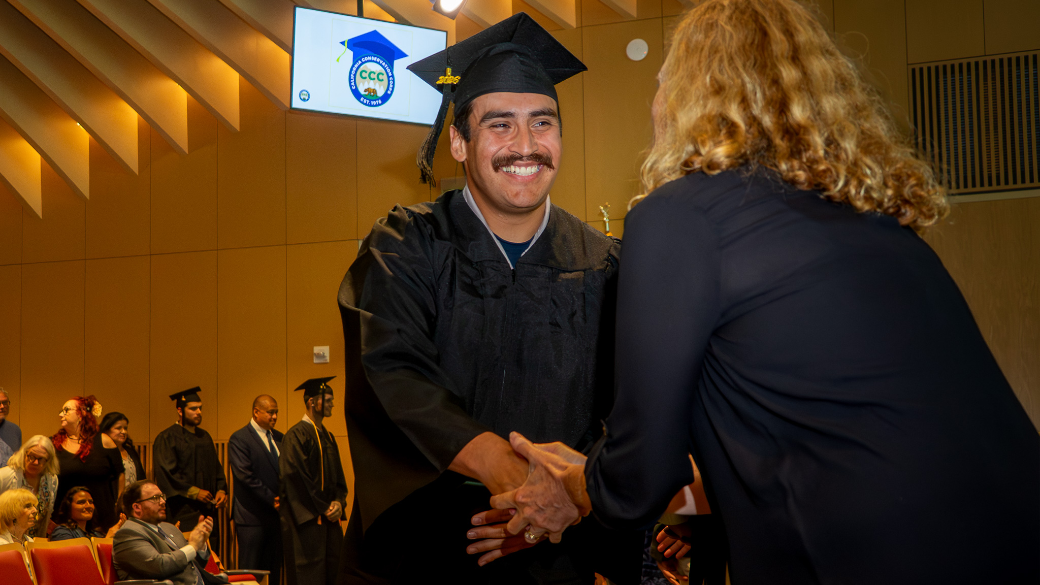 A CCC Corpsmember shakes hands with his teacher during a graduation ceremony.