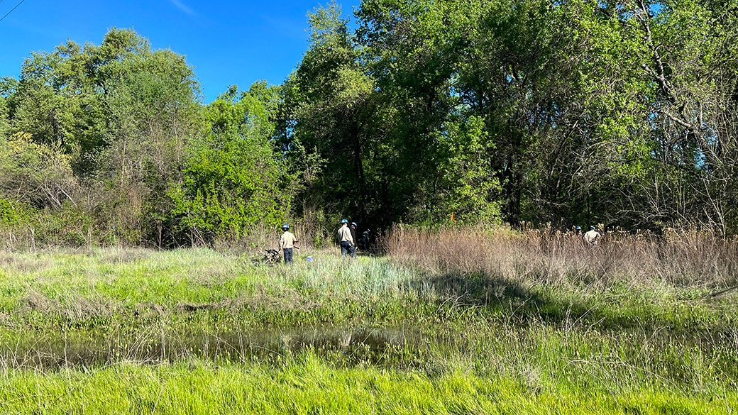 corpsmembers working off in distance of meadow near water source
